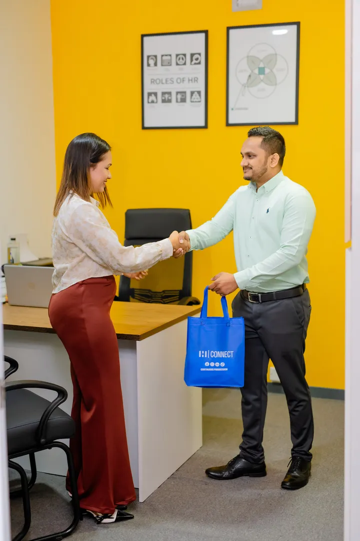 A Female employee greeting a male visitor with a handshake and a branded gift bag at H connect office