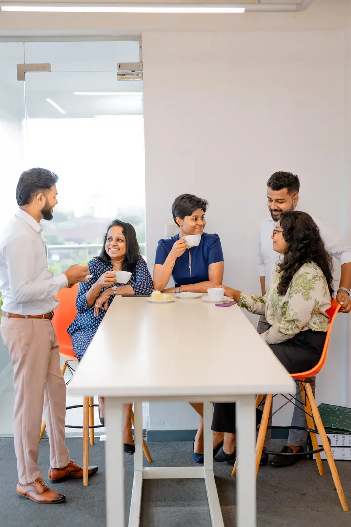 H connect employees having a casual coffee chat around a white table in a bright office