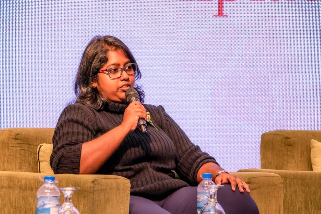 A female h connect employee sitting on a sofa on a stage reading to talk to a mic